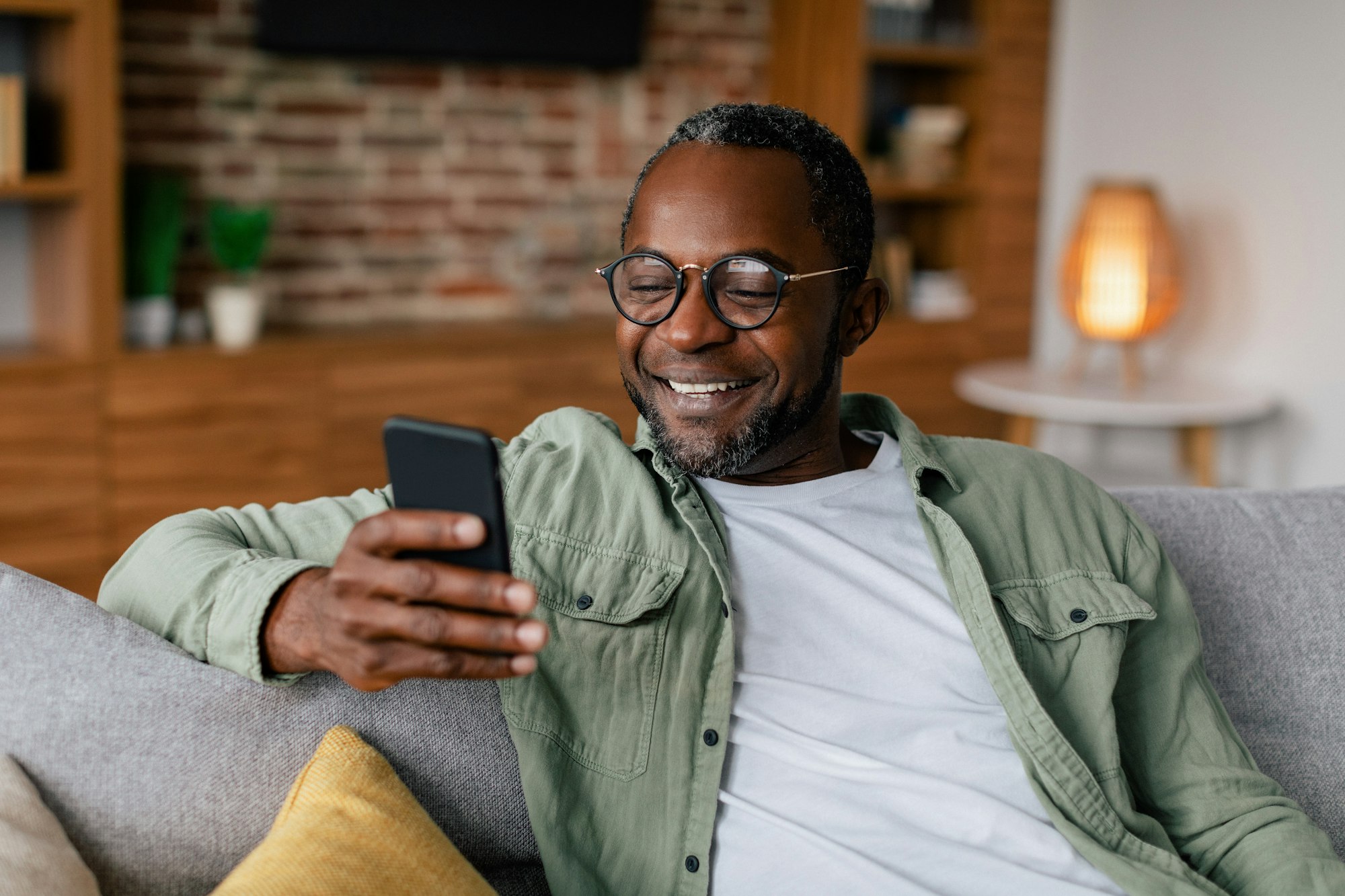 Cheerful middle aged african american male in glasses and casual chatting on smartphone, resting on